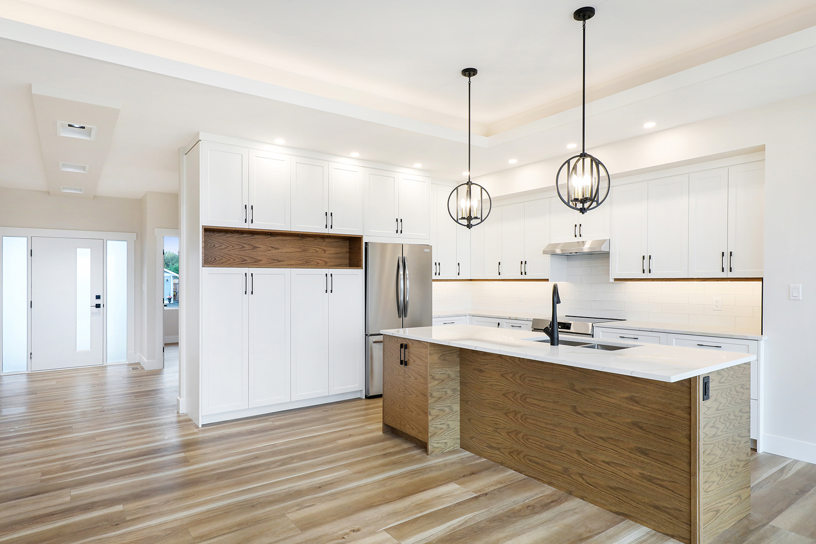 Interior of a white, modern kitchen with island. Wood and black matte metal furnishings with white cabinetry.